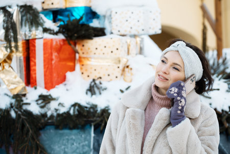 Beautiful young woman in a fur coat and mittens talking on the phoneの写真素材