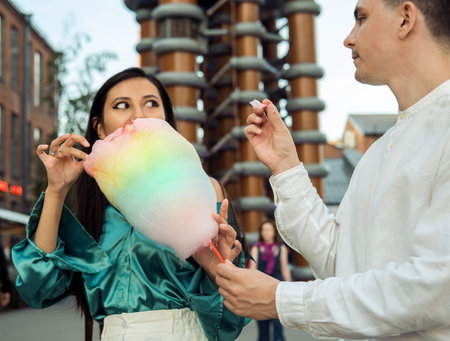 Beautiful young smiling couple walking down the street eating cotton candy and having great summer...