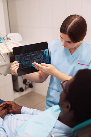 Young female dentist doctor showing dental treatment result demonstrating teeth xray shot during...