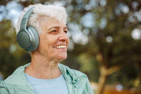 Old woman in headphones listens to music in the parkの写真素材