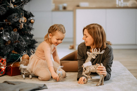 A young mother and little daughter play sitting near the Christmas tree. Family, winter holidays and people concept.の写真素材