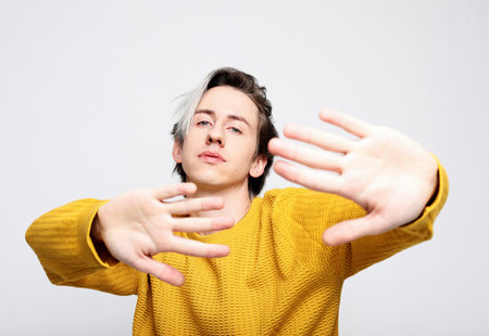 Stylish fashionable young man wearing yellow sweater dancing to the music over gray backgroundの写真素材