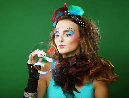 Young woman with creative make-up blowing soap bubbles over green background. Doll style.の写真素材