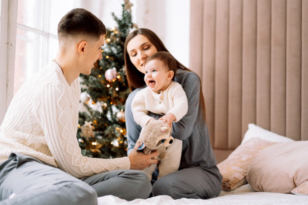 Happy young family - mom and dad together with little daughter next to christmas tree, have fun,...
