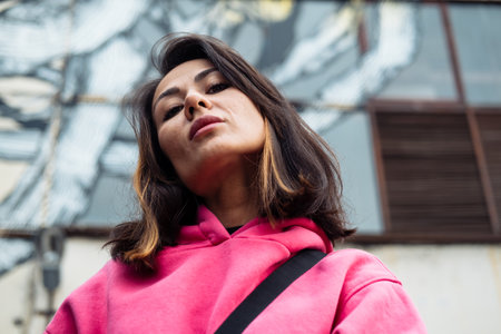Beautiful stylish Asian young woman in pink sweatshirt and jeans posing while looking at the camera,...