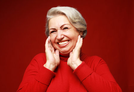 A cheerful old woman in a red sweater laughs and rejoices. Portrait on a red background. Lifestyle...