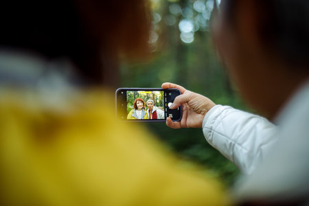 Multiracial elderly women having fun during trekking day in to the wood and make selfie with...