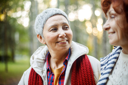 Happy senior couple women looking at each other walking in the forest. Caucasian active elderly gray haired people enjoying vacation freedom and nature hiking in footpath in a sunny dayの写真素材