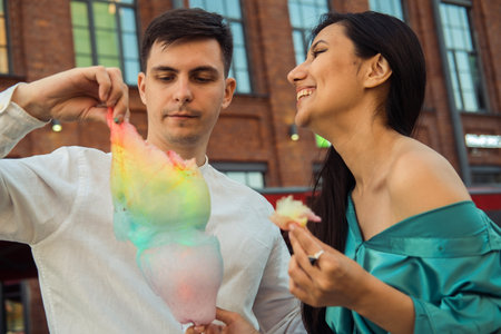 A cheerful couple in love walks in the city and eats cotton candy. Young Asian woman with long hair and European man. summer day.の写真素材