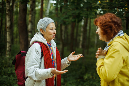 Lifestyle, emotion and female friendship concept. Cheerful pensioner female friends tallking and laughing in the autumn park.の写真素材