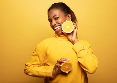 young happy afro american woman hold orange slices look amazed isolated on yellow color background.の写真素材