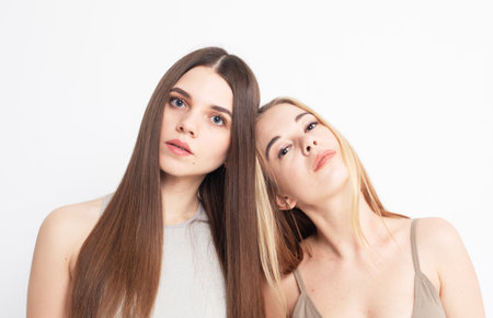 Two young women with long hair stand together on a white background, pose, look at the camera, lifestyle concept.の写真素材