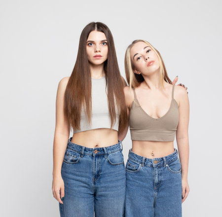 Two young women with long hair stand together on a white background, pose, look at the camera, lifestyle concept.の写真素材