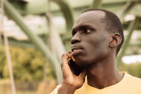 Serious black man calling on smart phone standing at the park. summer season.の写真素材