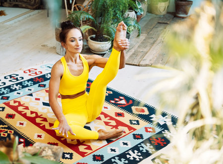 Brunette woman practices yoga at home among flowers. Urban jungle and gymnastics, yoga, pilates concept.の写真素材