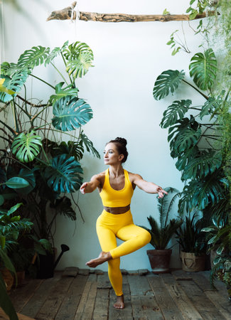 Adult woman practices yoga among the urban jungle. Female in yoga asanas and Pilates at home. lifestyle concept.の写真素材