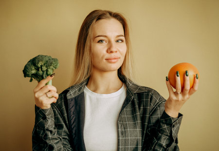 Inspired happy millennial woman show broccoli and orange. Sports, weight loss and body care, choice of harmful and healthy foodの写真素材