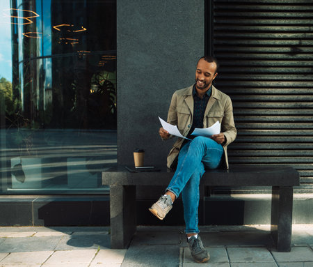 A young African American man sits at a bus stop and reads documents. lifestyle concept.の写真素材