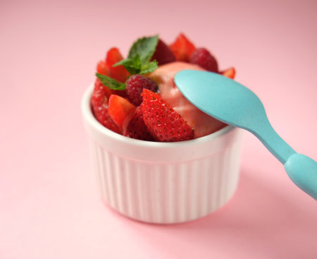 Strawberry ice cream and blue spoon over pink background, top viewの写真素材