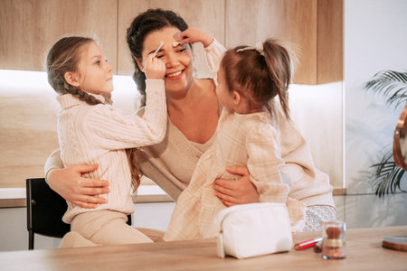 Two little girls sisters play with their mother using cosmetics. makeup game. happy time at home. lifestyle concept.の写真素材