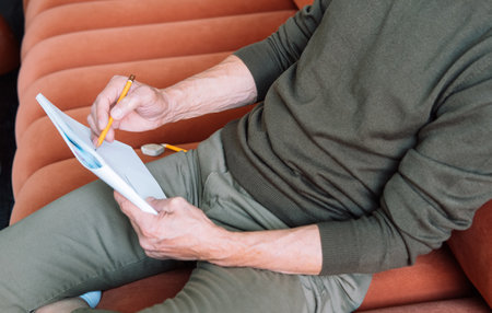 man dressed casually sits on the sofa and makes sketches in a notebook. close up.