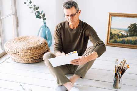A man holds an album and a pencil, makes sketches. The man is gray-haired and dressed casually, creativity in adulthood. lifestyle concept.の写真素材
