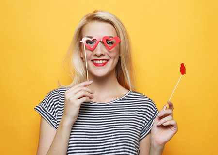 Party image. Young woman holding a party glasses over yellow background.の写真素材