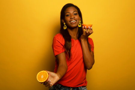 young afro american woman hold orange slices look amazed isolated on yellow color backgroundの写真素材
