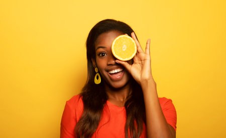 young afro american woman hold orange slices look amazed isolated on yellow color backgroundの写真素材