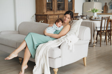 A young happy mother is sitting on the sofa and holding a baby in her arms. Childhood and family concept.の写真素材