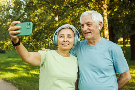 Happy active senior couple taking selfie sitting in park outdoors. Love togetherness and active seniors vitality conceptの写真素材