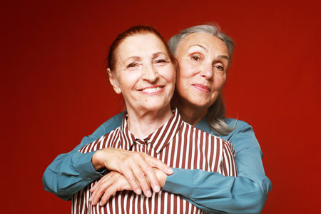 Two elderly women friends hugging on red background.の写真素材