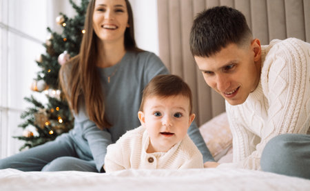 Young family with a baby, lie on the bed, have fun. Concept of childhood, love and family.