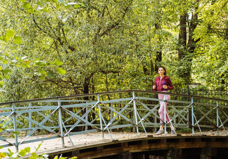Young sporty woman running on the bridge in autumn park.の写真素材