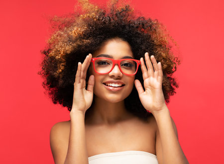 Happy Afro woman wearing eyeglasses smiling, has good mood isolated on studio red background.の写真素材