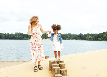 A young mother plays with her daughter on the beach near the lake. Lifestyle and family concept.の写真素材