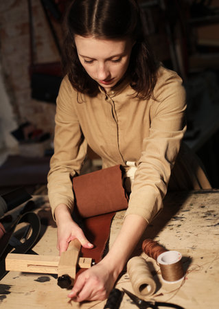young woman works in a workshop, sews leather bags