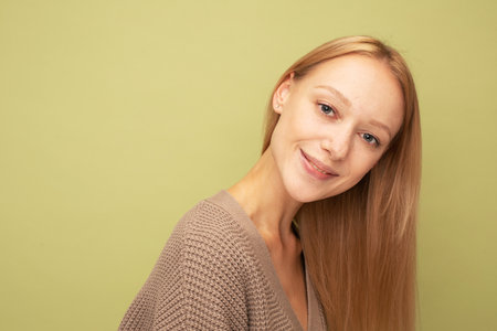 Portrait of cheerful young woman with blond hair smiling isolated over olive color backgroundの写真素材