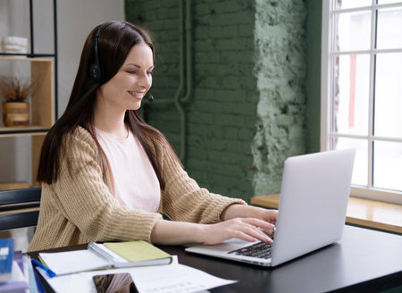 Young cheerful woman with long hair works on a modern laptop in her home office.