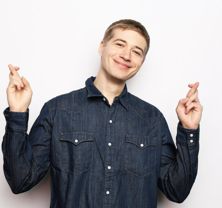 lifestyle, body language and people concept: Happy handsome man with crossed fingers over white backgroundの写真素材