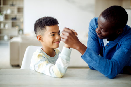 Happy african american father competing in arm-wrestling with his son, enjoying time together at home. Lifestyle concept.の写真素材
