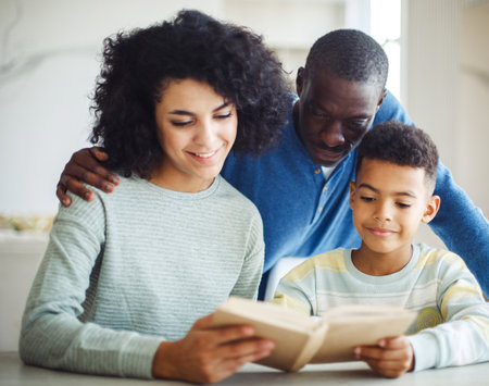 Young african american mother hold story book reading teaching little boy in living room. Father smiling. Home school learn from teacher, education happy family.の写真素材