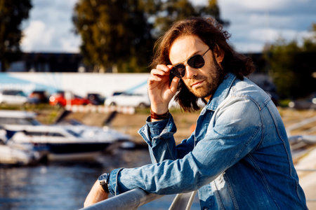 Stylish handsome male model with long hair posing near river on a summer day. Fashion and lifestyle concept.の写真素材