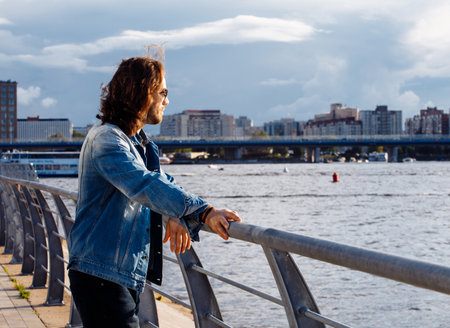 Stylish handsome male model with long hair posing near river on a summer day. Fashion and lifestyle concept.の写真素材