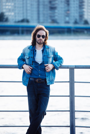 Stylish handsome male model with long hair posing near river on a summer day. Fashion and lifestyle concept.の写真素材