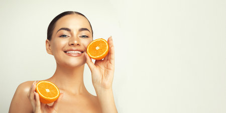 portrait of a lovely young woman standing isolated over white background, showing slices of an orangeの写真素材