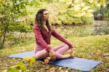 Young woman wearing pink clothes doing yoga exercise outdoor in the park near lake, sport yoga...