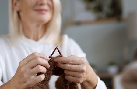 For my children. Happy delighted aged woman holding knitting needles and smiling while making a scarfの写真素材