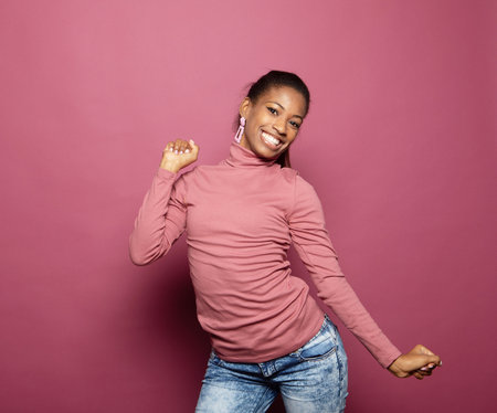 pretty smiling young afro woman dancing isolated pink color backgroundの写真素材