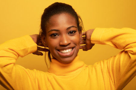 Close up portrait of beautiful young African woman laughing over yellow background, lifestyle and...